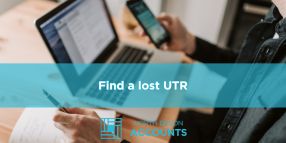 Find a lost Unique Taxpayer Reference Person checking paperwork while using a phone and laptop, illustrating how to find a lost Unique Taxpayer Reference with guidance from North Devon Accounts<br />